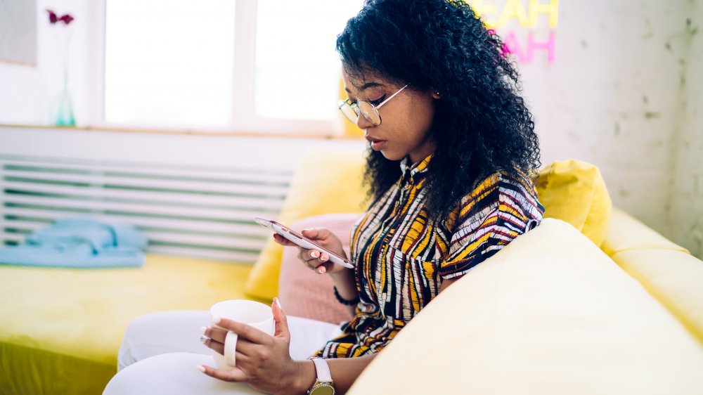 A woman drinking black tea and reading on her phone