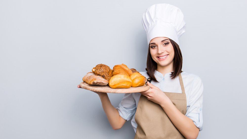 A woman in a chef had with a tray of breads