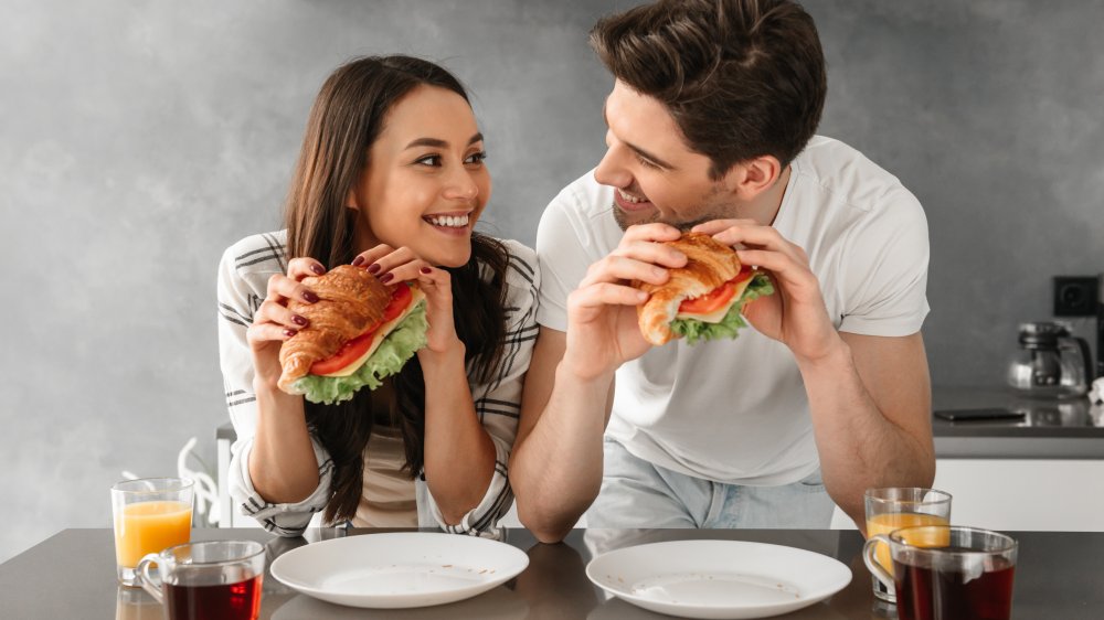 Man and woman eating deli meat sandwiches 