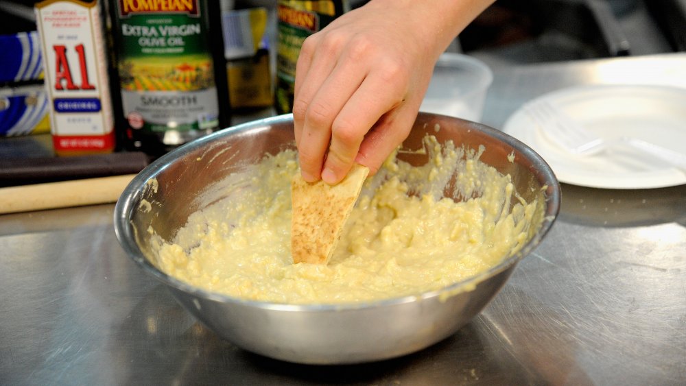 Person digging into a bowl of fresh hummus