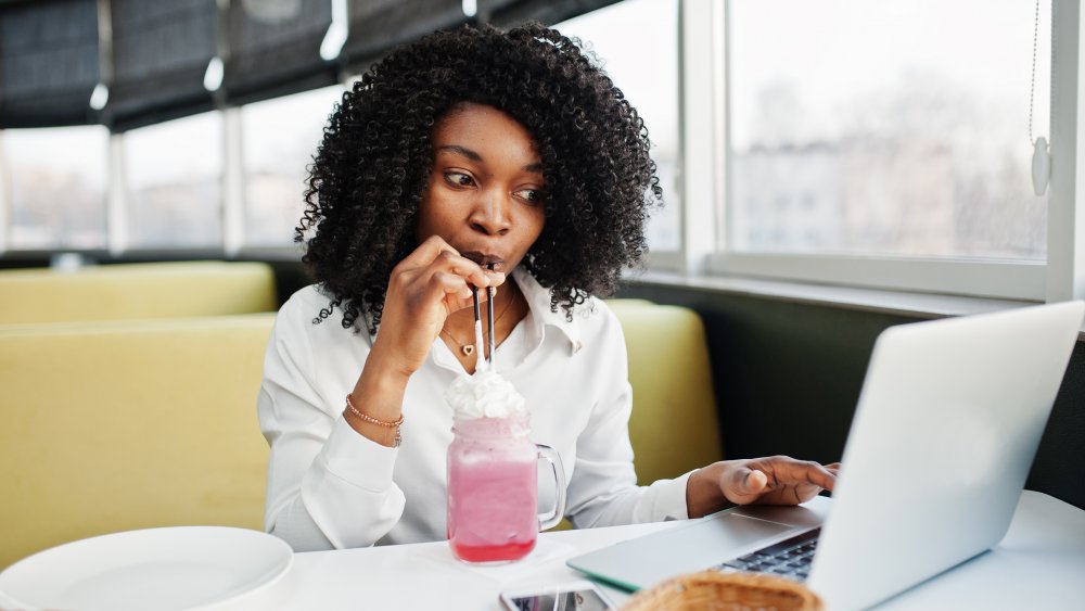 A woman on her laptop at a cafe drinking a milkshake with Splenda