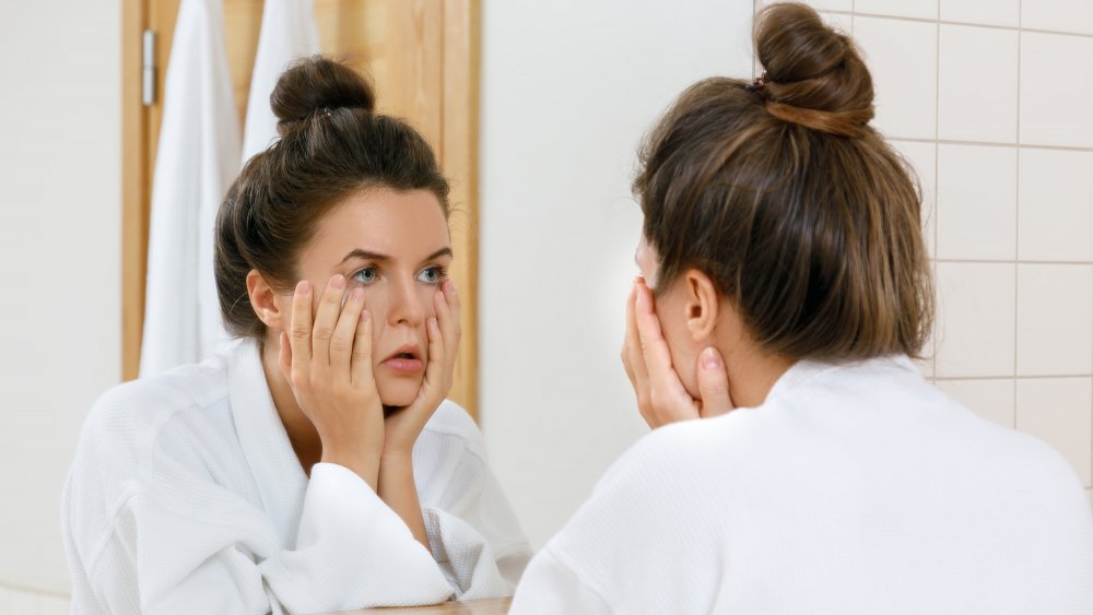 woman with a hangover looking into bathroom mirror