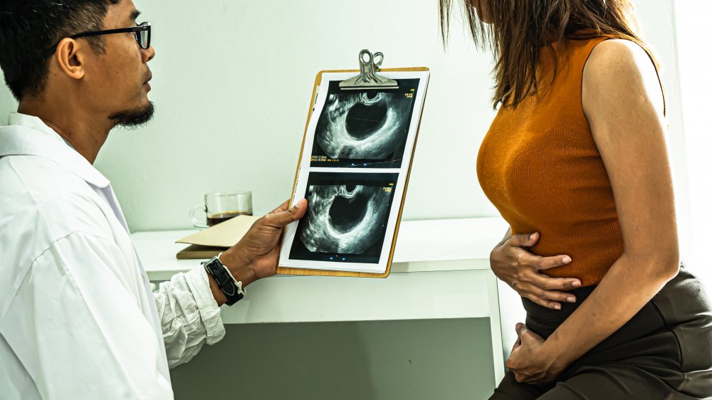 Doctor holding sonogram image next to woman touching her abdomen 