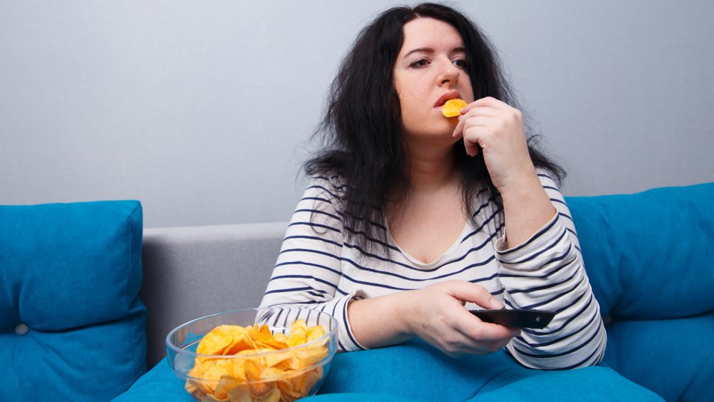 woman eating chips and watching TV on the couch