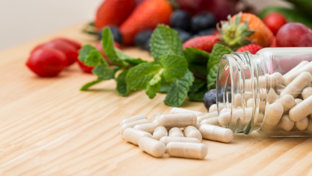 Vitamins pouring out of a bottle with herbs and fruit in the background