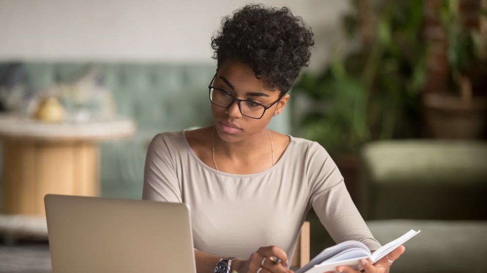 A woman focusing on her laptop with a book