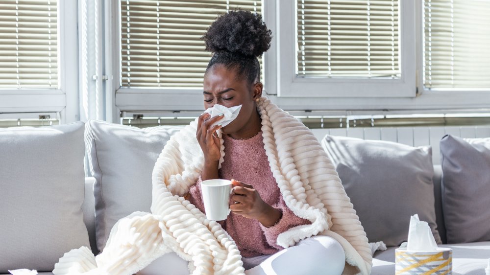 A sick woman sitting on a couch blowing her nose