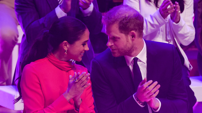 Meghan Markle and Prince Harry smiling at each other clapping