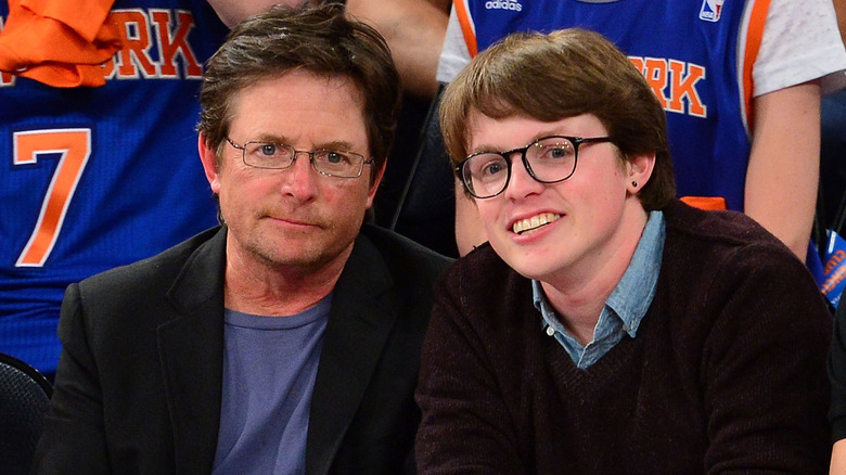 Michael J. Fox and Sam Michael Fox sitting in front of people wearing New York Knicks jerseys