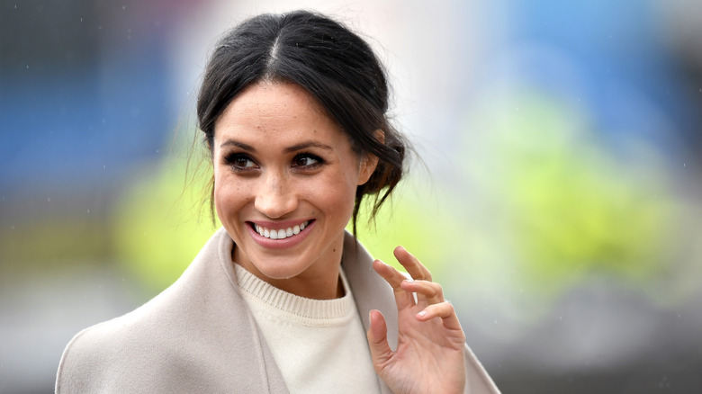 Meghan Markle wearing a sweater, smiling and waving