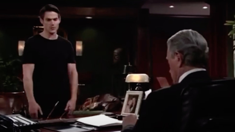 Adam stands in front of Victor's desk