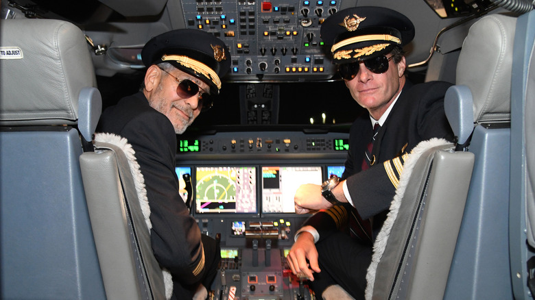 George Clooney and Rande Gerber in pilot outfits sitting in the cockpit of a plane