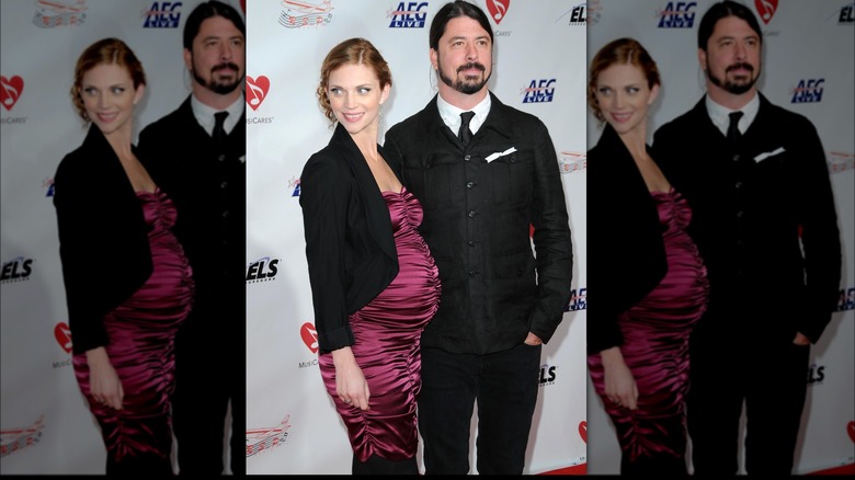 A pregnant Jordyn Blum in maroon dress and black jacket with Dave Grohl in black suit and ponytail