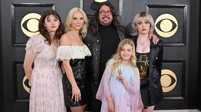 Robyn Blum in black and white dress and Dave Grohl in black shirt and glasses with their three daughters