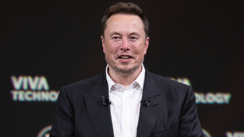 Elon Musk in a black suit speaking at an event