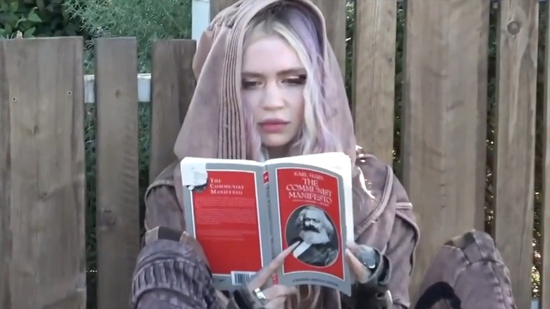 Grimes sitting by a fence reading The Communist Manifesto