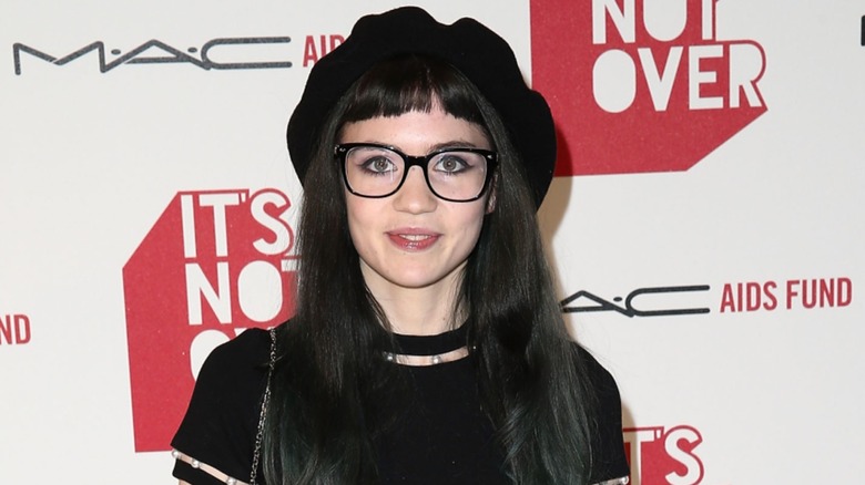 Grimes smiling in a beret and black glasses on a MAC Aids Fund step-and-repeat