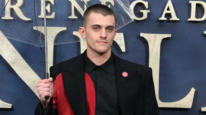 Jake Dunn holding a clear umbrella while posing for photos in a black and red suit