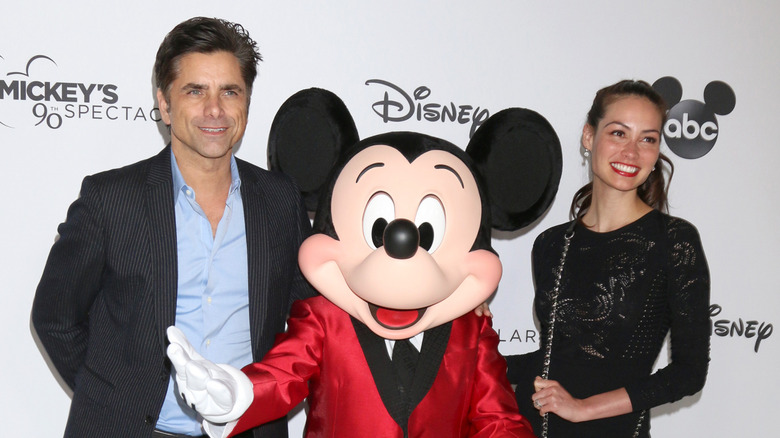 Caitlin and John Stamos stand on red carpet with Mickey Mouse between them