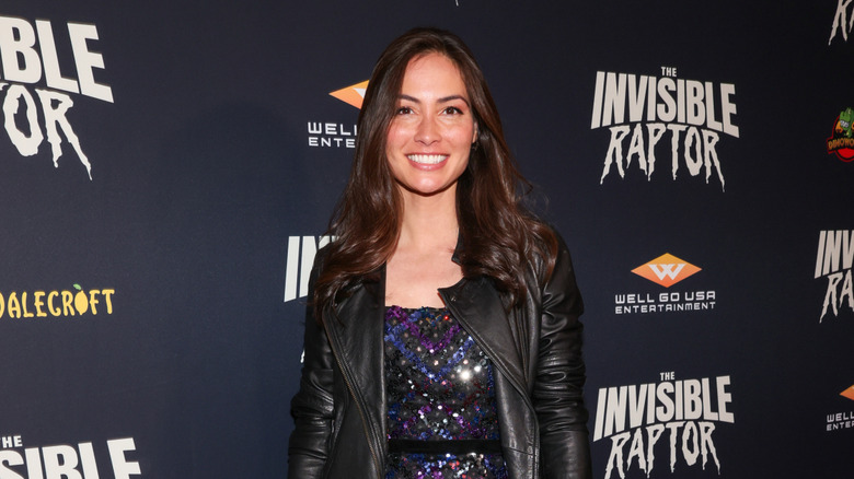 Caitlin McHugh attends premiere smiling on red carpet in a leather jacket and sequin dress