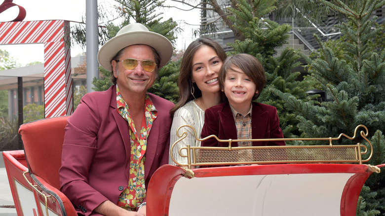 Caitlin and John Stamos sit in sleigh with son Billy outside smiling