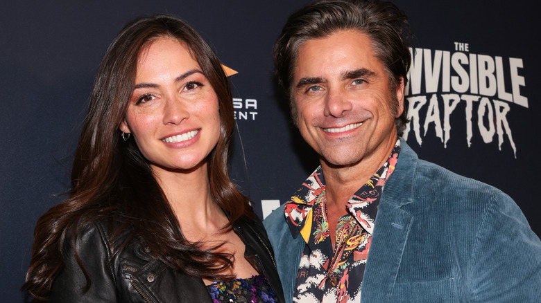 Caitlin McHough stands next to John Stamos smiling at The Invisible Raptor premiere.