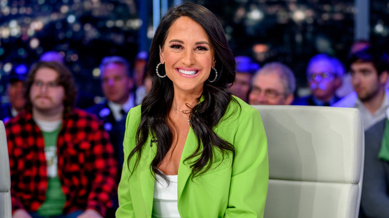 Emily Compagno smiling in green suit on air at Fox with audience behind her