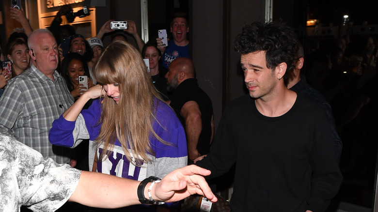 Taylor Swift and Matt Healy walking by a crowd