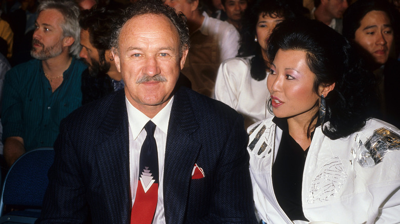 Gene Hackman looking thoughtful while Betsy Arakawa talks to him