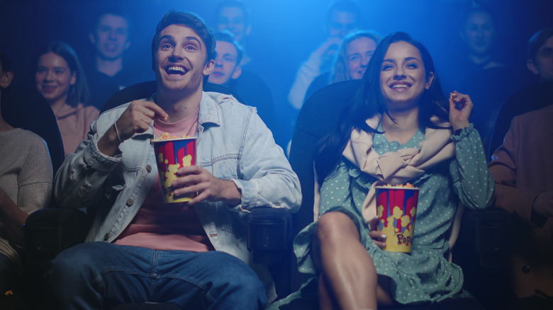 couple eats popcorn and laughs in a movie theater