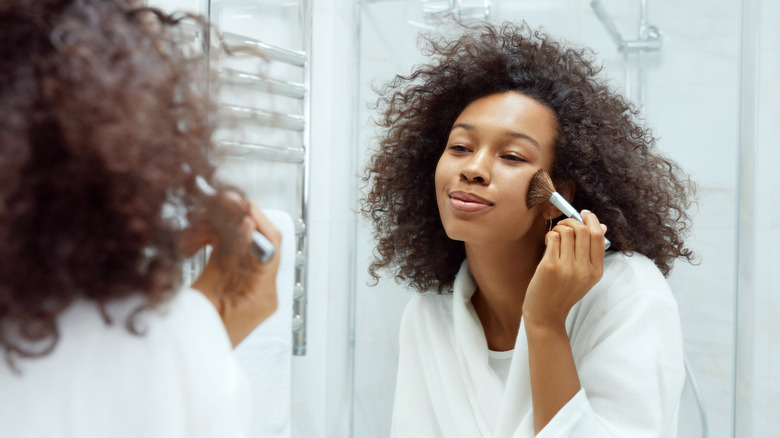 Woman applying makeup with brush in mirror