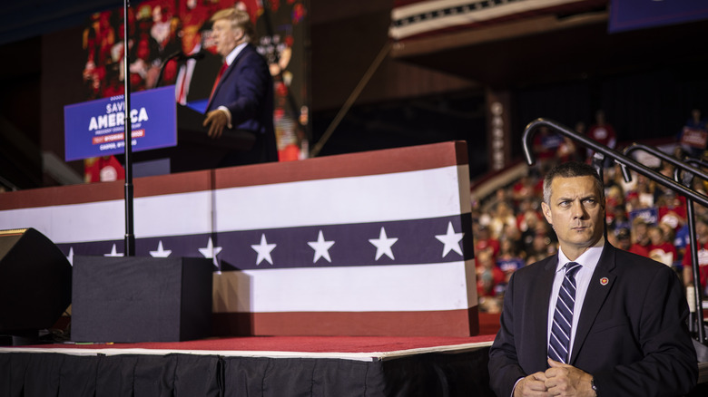 Security guard looks into crowd while Donald Trump speaks at podium behind him