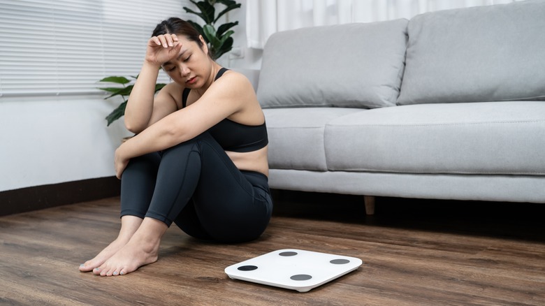 woman looking sadly at a scale 