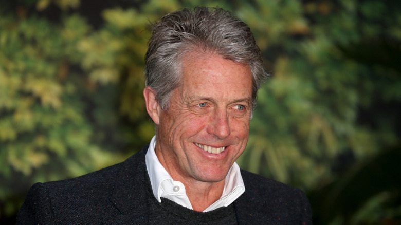 Hugh Grant smiling, sporting gray hair and wrinkles