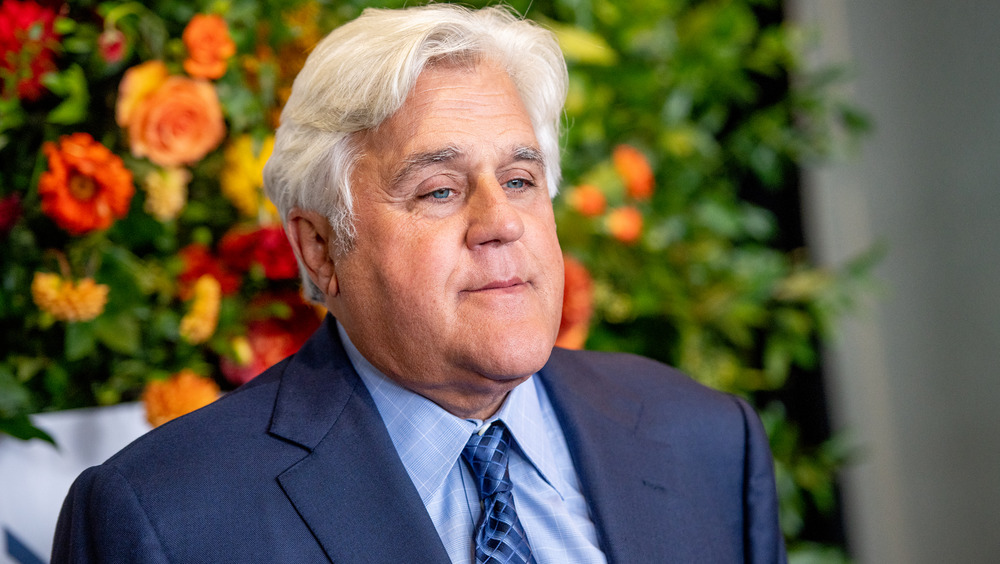 Jay Leno wearing a suit by a floral background