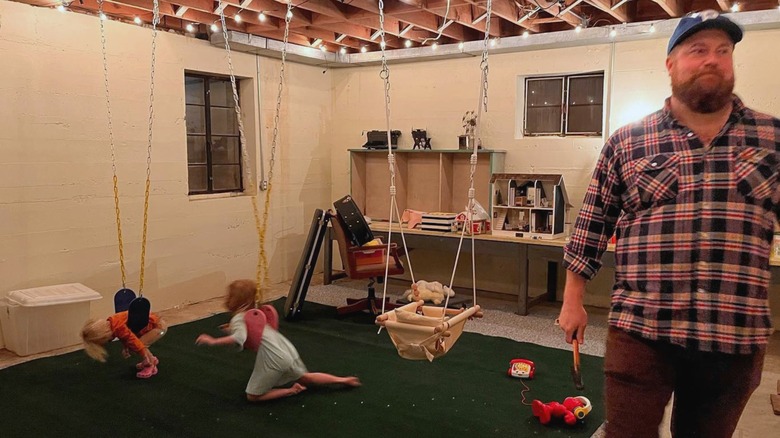 Helen and Mae Napier play on indoor swings, Ben Napier walks by with tools in hand