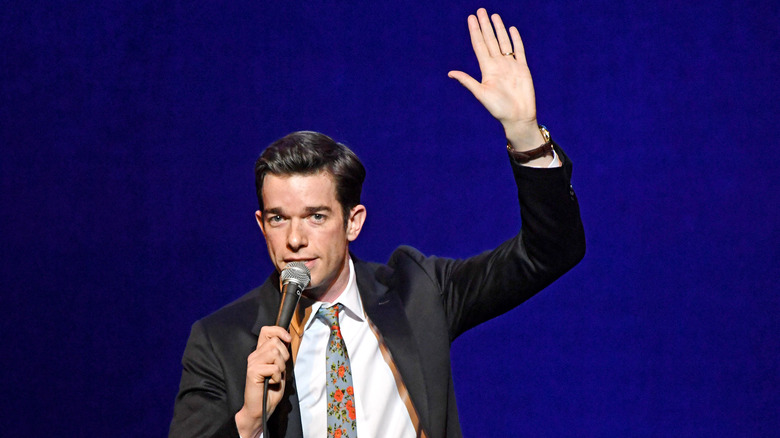 John Mulaney performs onstage with hand in air