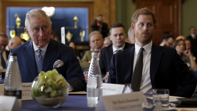 King Charles III and Prince Harry sitting stony-faced at an event