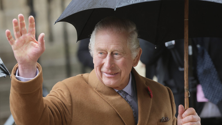 King Charles III waves at crowd holds umbrella