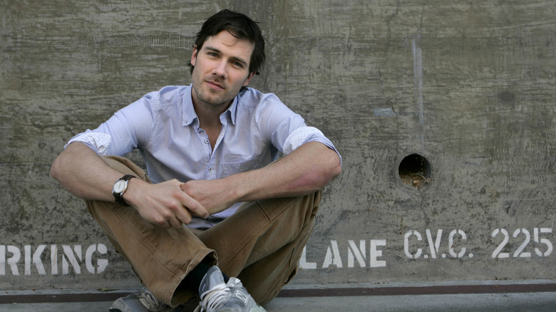 Luke MacFarlane sitting against concrete