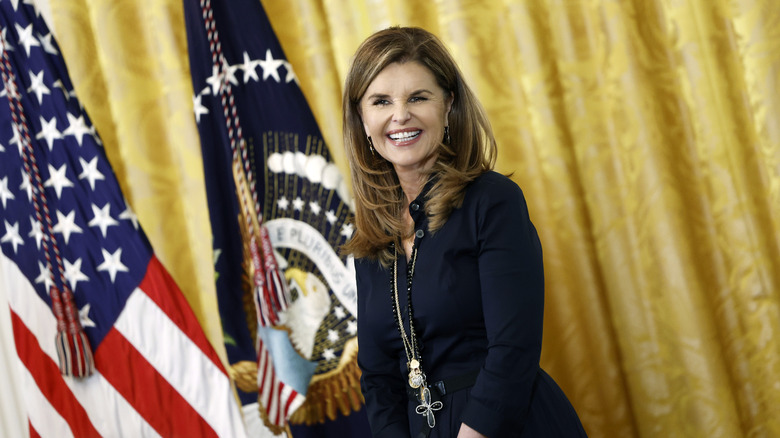 Maria Shriver smiling next to American flag