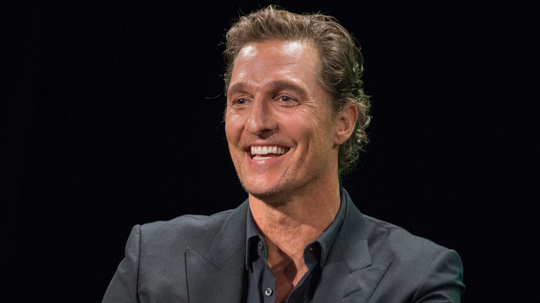 Matthew McConaughey smiling onstage in a grey suit