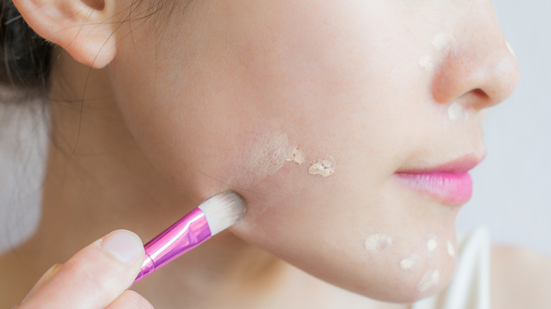 woman using makeup brush to conceal blemishes