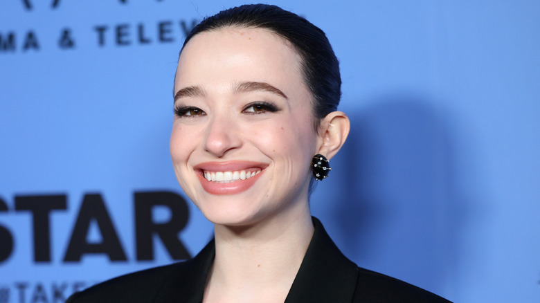 Mikey Madison smiling against blue background on step-and-repeat