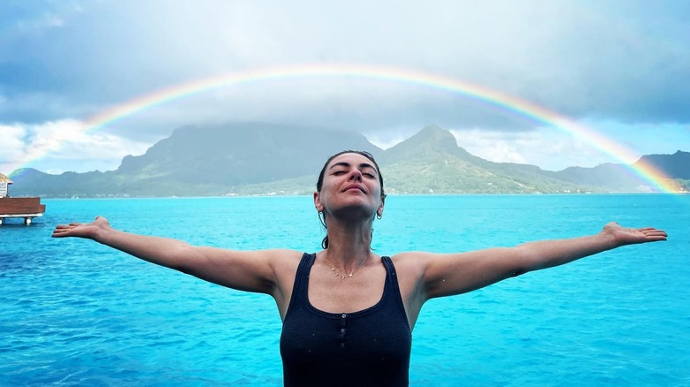 Mila Kunis posing by the sea with a rainbow