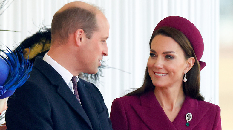 Kate Middleton smiling at Prince William and wearing emerald Princess of Wales pin