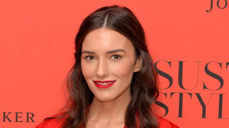 Kick Kennedy on red carpet, wearing red dress and red lipstick, smiling at camera.