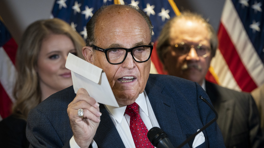 Rudy Giuliani holds a mail-in ballot while speaking about the lawsuits filed over the 2020 election.