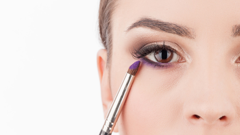 Person applying purple eyeshadow to undereye