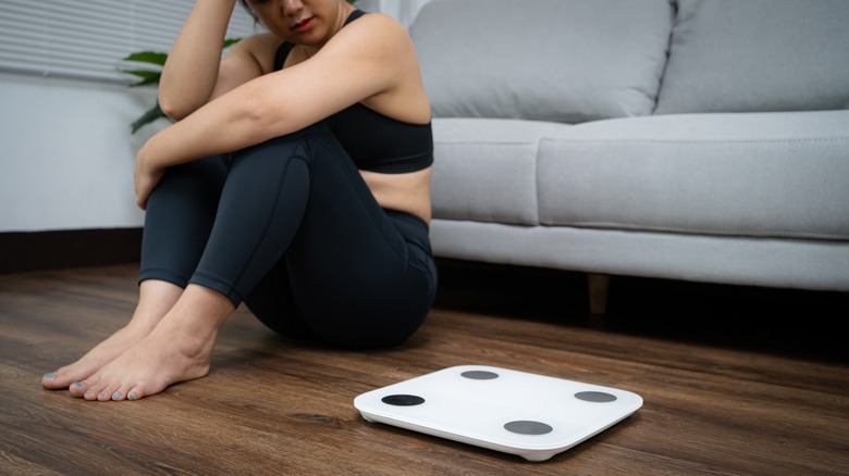 woman sitting next to a scale looking upset